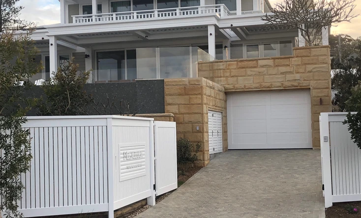 a driveway with a white fence and a stone wall